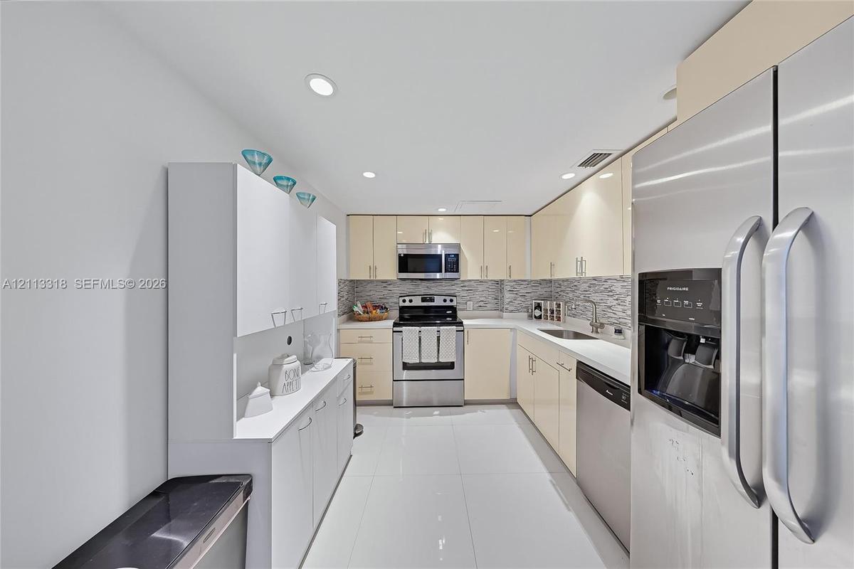 Kitchen featuring glossy cabinetry, stainless steel appliances, tile backsplash, polished stone countertops, and tile flooring
