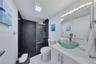 Bathroom featuring a walk-in shower with dark horizontal tile surround, glass vessel sink, white vanity, and wall-mounted light fixture
