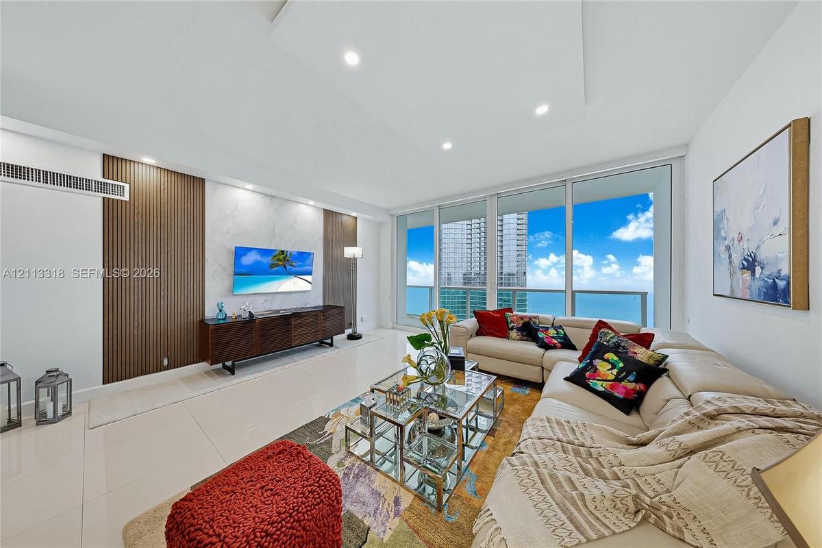 Living area featuring floor-to-ceiling windows, porcelain tile flooring, recessed ceiling lighting, and a decorative wall treatment with vertical wood