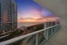 Covered balcony with a glass panel railing, tile flooring, and expansive ocean and coastal scenery