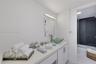 Bathroom featuring a solid-surface countertop, glass vessel sink with brushed-finish faucet, white cabinetry with silver-tone hardware, and a tub-show