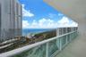 Covered balcony featuring tile flooring and a glass-paneled railing overlooking the coastline and ocean