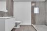 Bathroom featuring a white vanity cabinet, rectangular white countertop basin, chrome faucet, glass-enclosed shower, and large-format grey tile floori