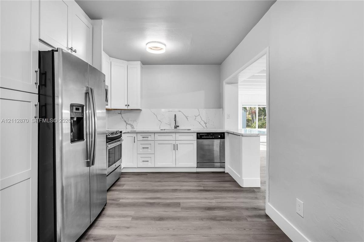 Kitchen featuring white shaker-style cabinetry, stone-patterned backsplash, stainless steel appliances, and wood-finish flooring