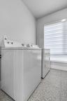 Utility space featuring speckled composite flooring, neutral wall tones, and a window with horizontal cellular shades