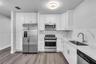 Kitchen featuring white shaker-style cabinetry, stone-patterned backsplash, stainless steel appliances, and wood-finish flooring