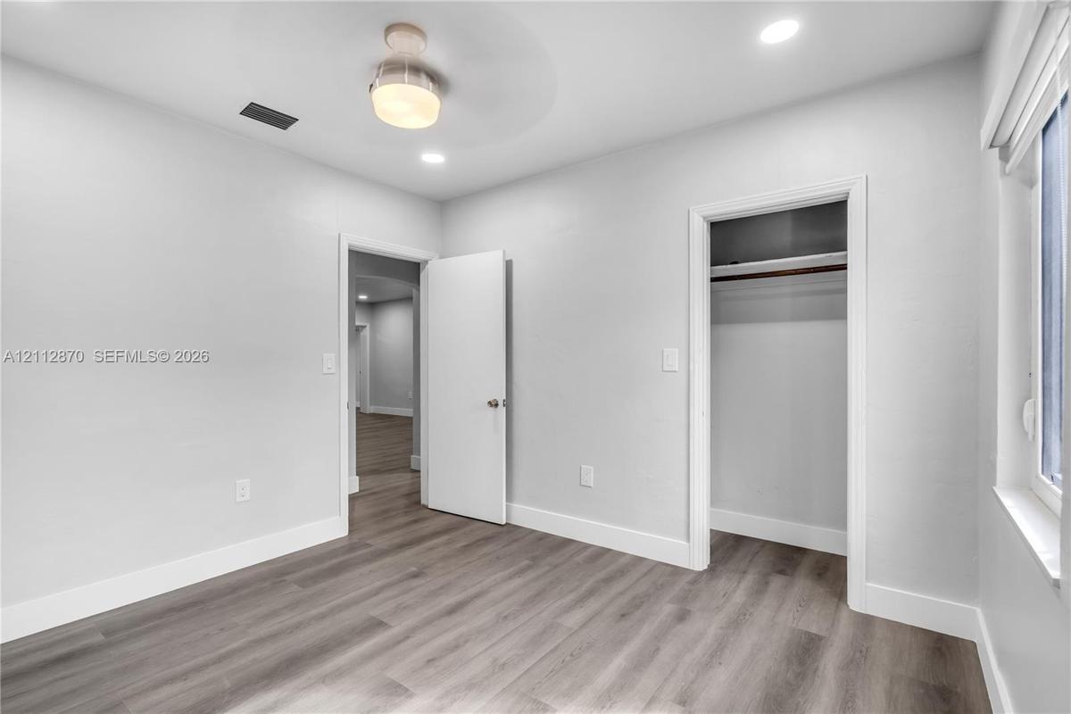 Neutral-toned interior space featuring wood-finish flooring, recessed lighting, a modern ceiling-mounted light fixture, and a reach-in closet