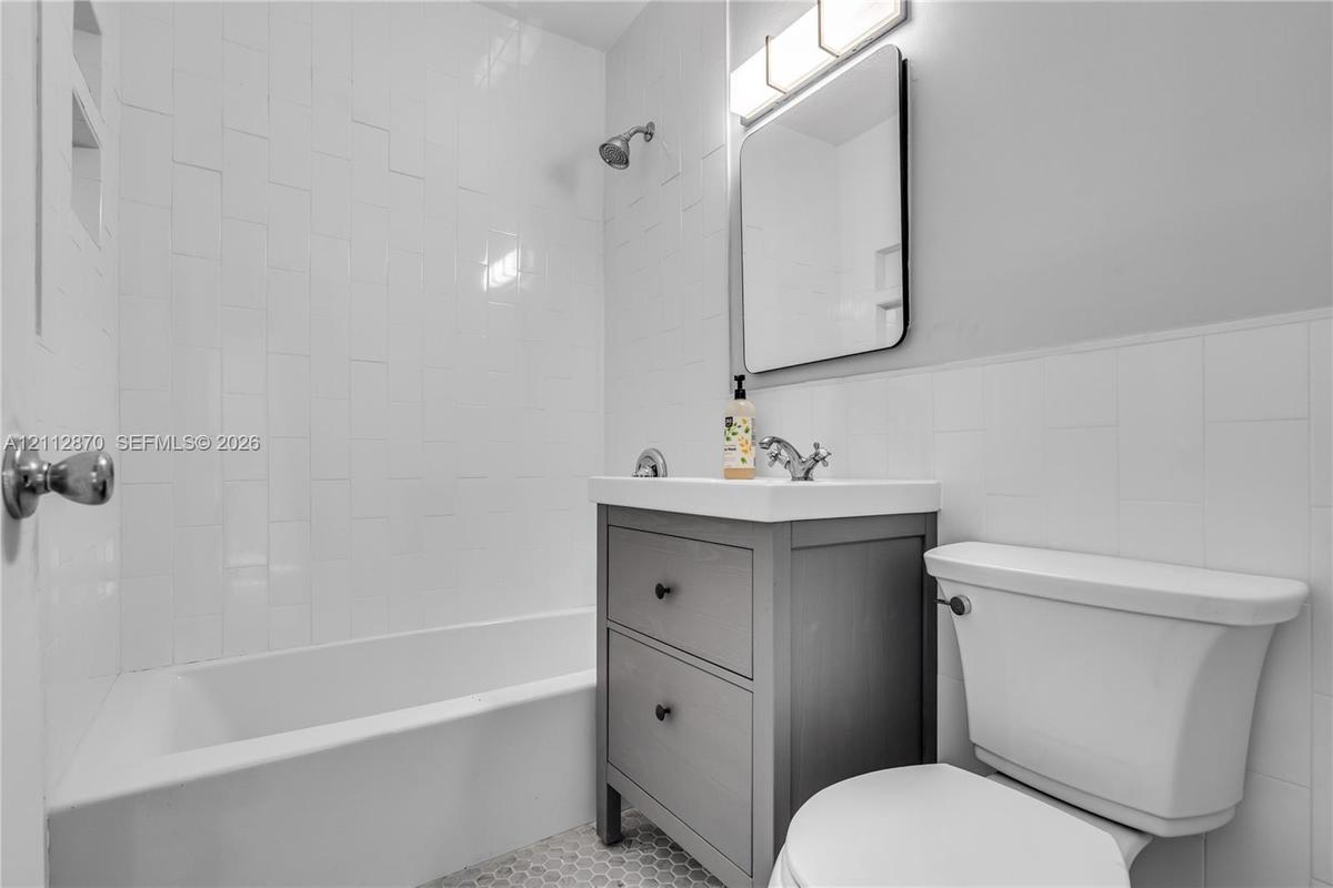 Bathroom featuring a vanity with two storage drawers, white subway tile shower surround, hexagonal floor tile, rectangular wall-mounted mirror, and th