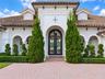 Stucco exterior featuring an arched entryway, double iron-detail glass doors, clay tile roof, and brick paver driveway