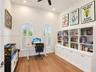 High-ceilinged room featuring wood-finish flooring, custom floor-to-ceiling built-in cabinetry, two arched windows with plantation shutters, and a cei