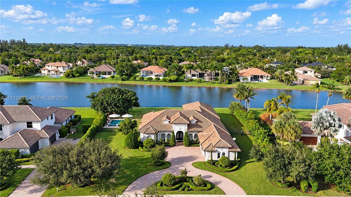 Waterfront residence featuring a tile roof, paved circular driveway, manicured landscaping, and a private swimming pool