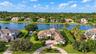 Waterfront residence featuring a tile roof, paved circular driveway, manicured landscaping, and a private swimming pool