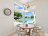 High-ceiling dining area featuring expansive corner windows, a multi-globe metal chandelier, and stone-finish flooring with outdoor water and pool acc