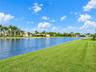 Waterfront lot featuring a large body of water, expansive manicured lawn, and mature palm trees