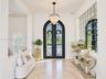 Foyer featuring arched double iron entry doors, light-toned stone flooring, a multi-tiered crystal chandelier, and an expansive grid-pattern wall mirr