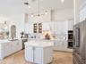 Kitchen featuring white shaker-style cabinetry, central island with stone-finish countertops, stainless steel double wall ovens, brick-pattern backspl