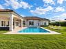 Stucco exterior with a tiled roof featuring a covered lanai, inground pool with an integrated spa, and expansive lawn