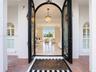 Arched double entry doors with decorative iron detailing, flanked by arched windows with plantation shutters, polished stone flooring, and a multi-tie
