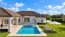 Rear exterior featuring a covered patio, a rectangular swimming pool with an integrated spa, stone-paver decking, and a manicured lawn