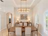 Tray ceiling with recessed lighting, tiered crystal chandelier, tile flooring, and arched windows featuring plantation shutters