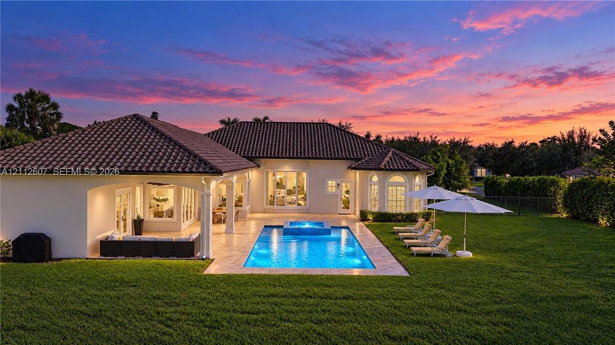 Rear exterior featuring a tile roof, stucco facade, stone-paved patio, custom swimming pool with integrated spa, and expansive lawn