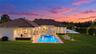 Rear exterior featuring a tile roof, stucco facade, stone-paved patio, custom swimming pool with integrated spa, and expansive lawn
