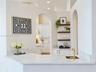 Built-in wet bar featuring stone-finish countertop, undermount sink with brass-finish faucet, and custom shelving, framed by architectural archways