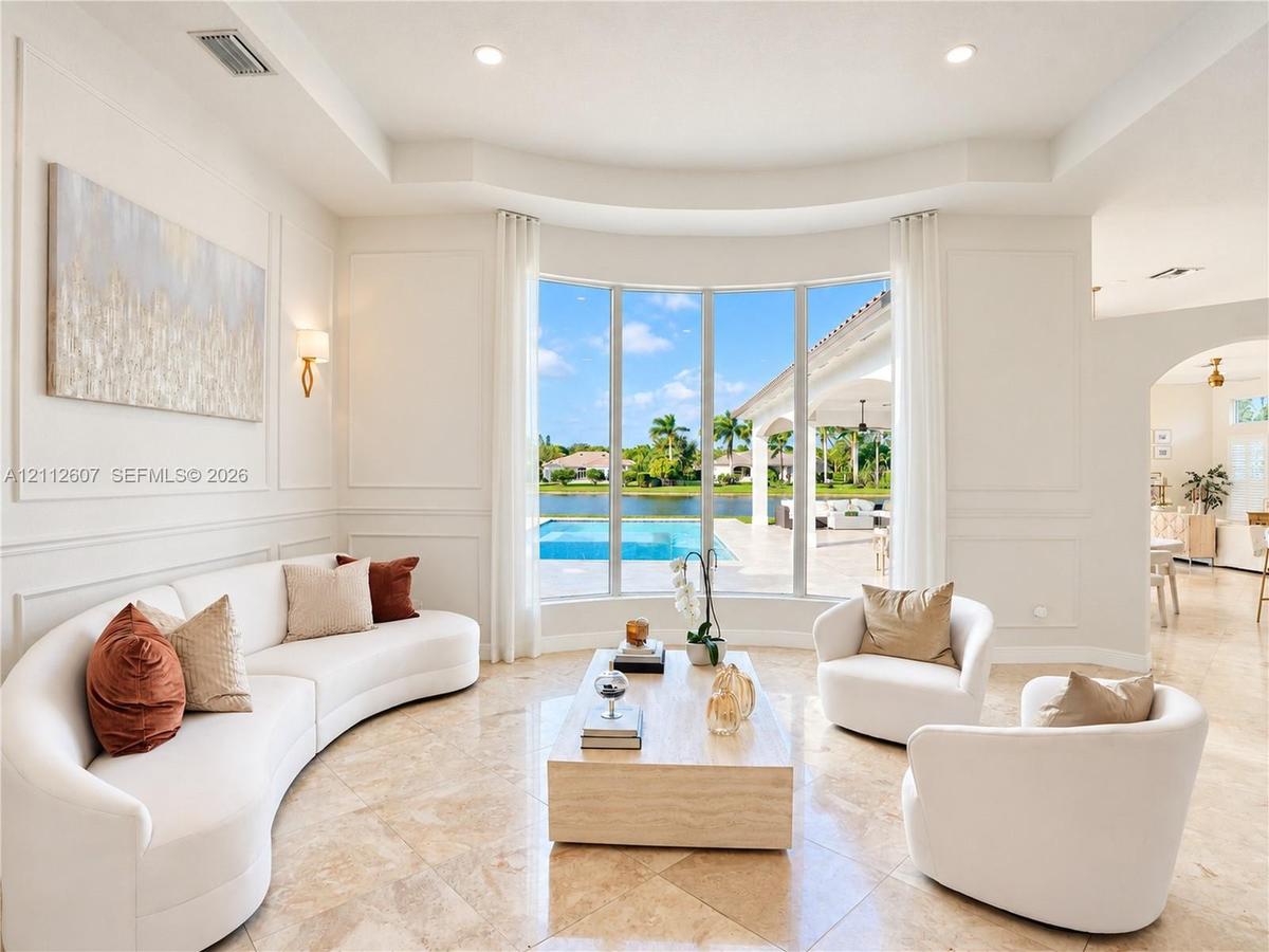 Living area featuring large bay windows, recessed ceiling, wall molding, polished stone tile flooring, and wall-mounted light fixtures