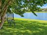Waterfront backyard featuring a manicured lawn, mature shade trees, and black metal perimeter fencing