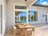 Covered lanai featuring neutral stone tile flooring, an integrated ceiling fan, expansive glass picture windows, and a curved architectural wall detai