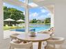 Floor-to-ceiling corner windows showcasing a paved pool deck, a swimming pool with integrated spa, and water frontage