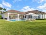 Rear exterior featuring a tile roof, covered patio with recessed lighting, in-ground pool with integrated spa, and expansive lawn