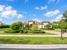 Stucco exterior featuring a clay tile roof, arched entryway, paved circular driveway, and manicured landscaping with shaped hedging