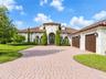 Mediterranean-style exterior featuring a paved stone driveway, arched entryways, tile roof, and multi-car garage with wood-finish doors