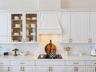 Kitchen featuring white cabinetry with glass-front uppers, a custom range hood, subway tile backsplash, solid-surface countertops, and gold-tone hardw