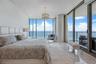 Floor-to-ceiling glass walls, stone flooring, cylindrical structural column, and a tiered crystal chandelier