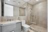 Bathroom featuring a gray vanity with a neutral stone-surfaced countertop, integrated sink, wall-spanning mirror, and a walk-in shower enclosed by a s