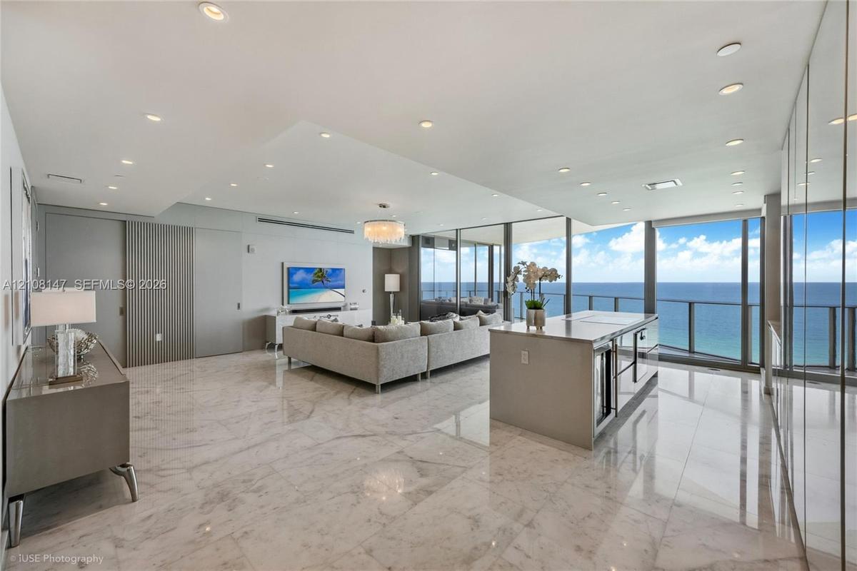Open-concept living space featuring polished stone flooring, floor-to-ceiling glass wall panels, an integrated kitchen island with stone countertop, r