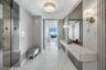 Foyer featuring polished stone flooring, custom wall-mounted floating console, mirrored wall panels, decorative wall sconces, and recessed drum ceilin