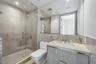 Glass-enclosed walk-in shower with floor-to-ceiling tile, high-gloss vanity with stone countertop, undermount sink, and full-width wall mirror