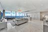 Open-concept interior featuring floor-to-ceiling glass panel walls, light-toned stone-finish flooring, recessed lighting, sleek high-gloss cabinetry, 