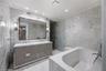 Dual-sink vanity with high-gloss cabinetry, stone-surround soaking tub, wall-to-wall stone tiling, and recessed lighting