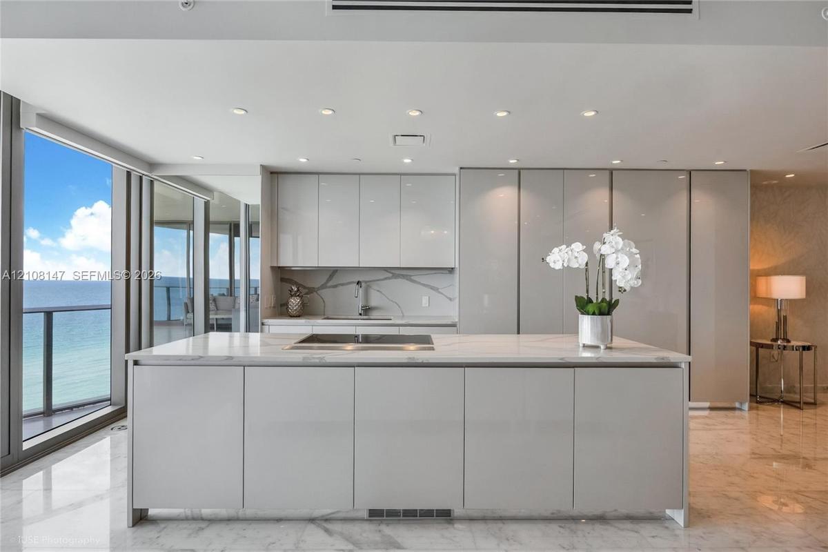 Kitchen featuring high-gloss cabinetry, stone-surface island with integrated cooktop, matching stone backsplash, polished tile flooring, and floor-to-