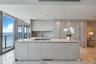 Kitchen featuring high-gloss cabinetry, stone-surface island with integrated cooktop, matching stone backsplash, polished tile flooring, and floor-to-