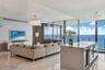 Open-concept interior featuring polished stone flooring, recessed lighting, a modern crystal chandelier, floor-to-ceiling glass panel walls, and a kit