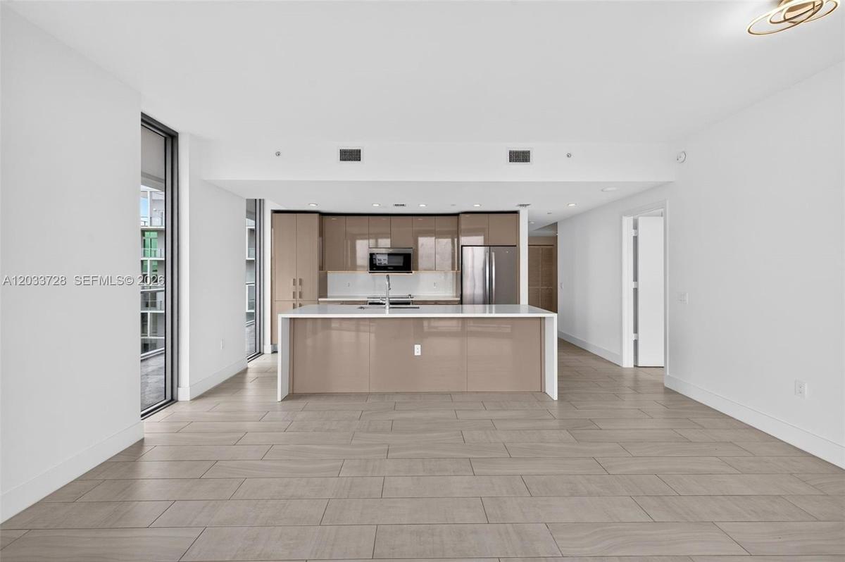 Contemporary kitchen featuring high-gloss cabinetry, a central island with a quartz countertop, stainless steel appliances, and large-format tile floo