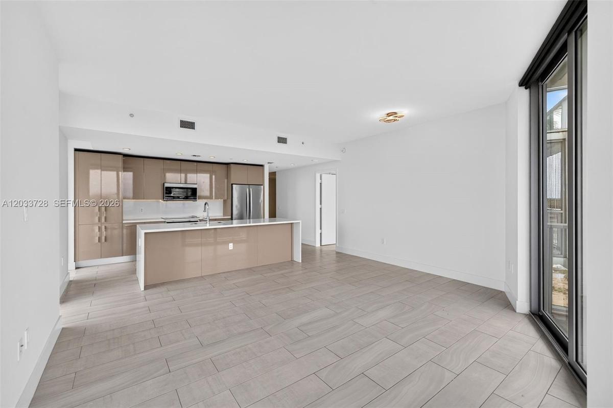 Open-concept kitchen featuring high-gloss cabinetry, a stone-surface island, stainless steel appliances, and large-format tile flooring
