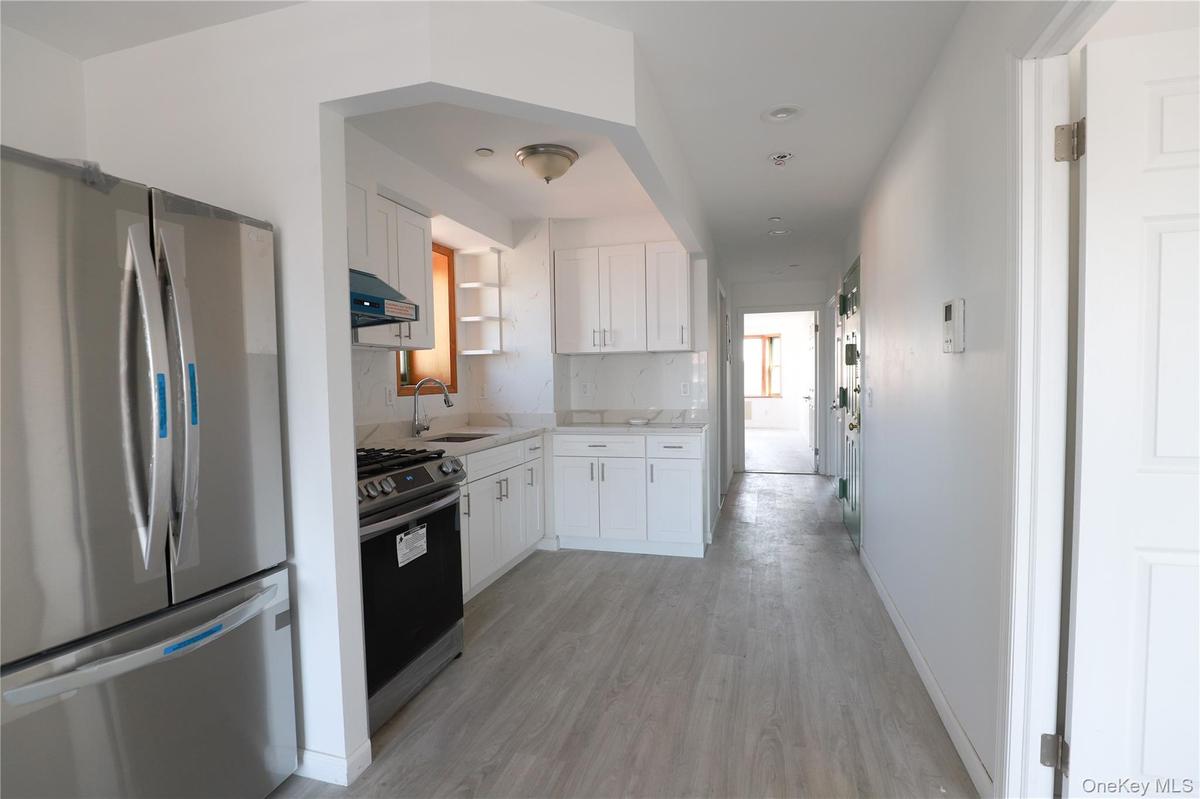 Kitchen featuring stainless steel refrigerator and range, white cabinetry, solid-surface countertops, and wood-finish flooring