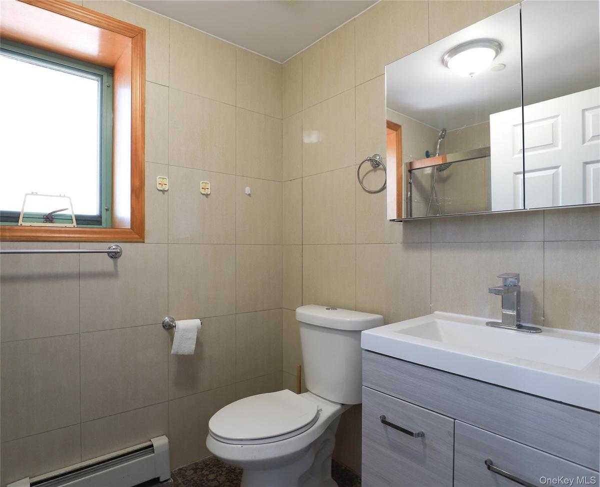 Bathroom featuring full-height wall tile, wood-finish vanity with an integrated sink, polished chrome faucet, and recessed medicine cabinet