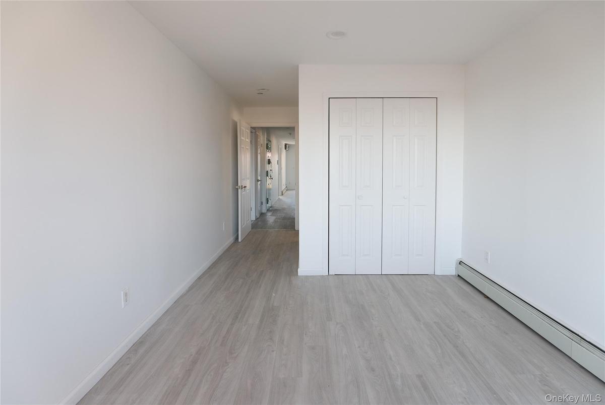 Neutral-toned interior featuring wood-finish flooring, white walls, and a built-in bifold closet